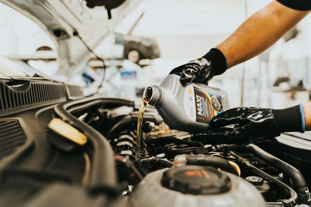 Close-up of a mechanic pouring engine oil into a car engine in an auto repair shop.