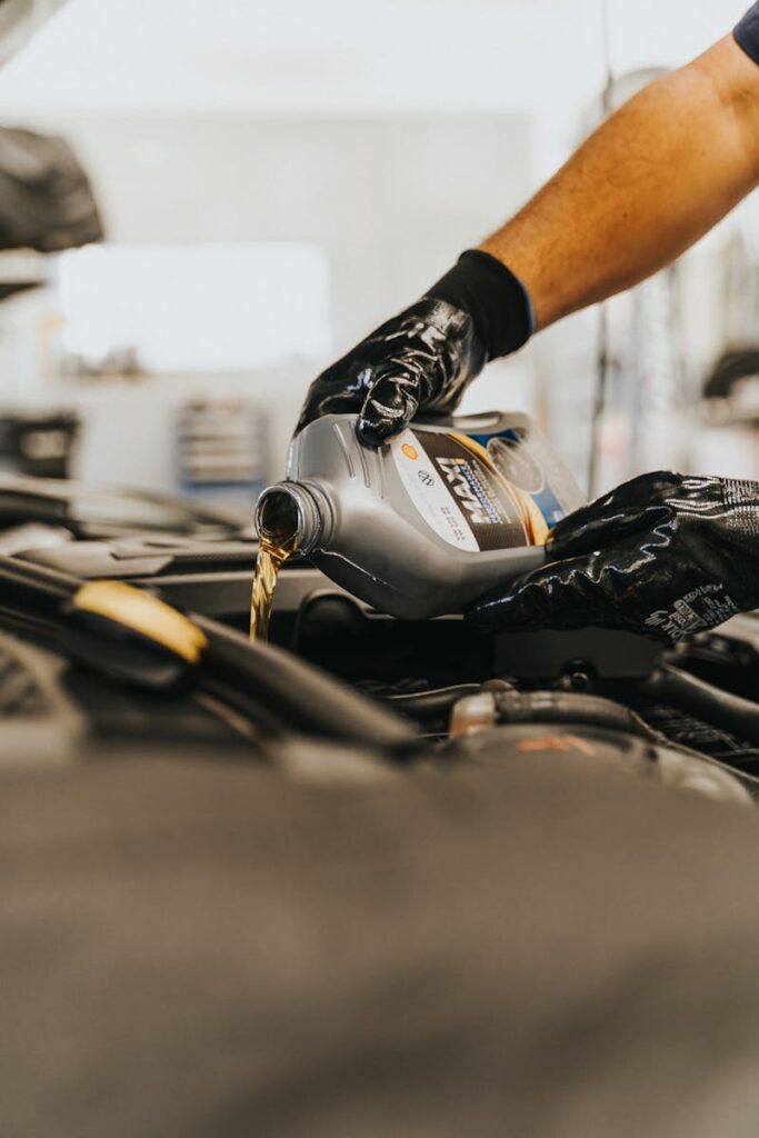 Close-up of a mechanic pouring engine oil into a car engine with gloved hands, indoors.