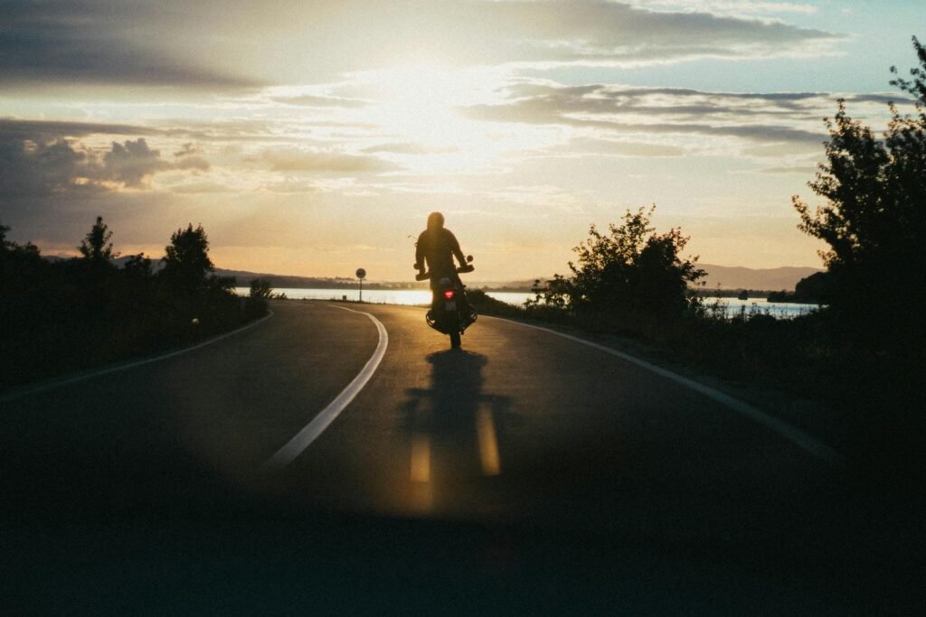 Silhouette of a motorcyclist riding on a scenic road during a beautiful sunset, emphasizing freedom and adventure.