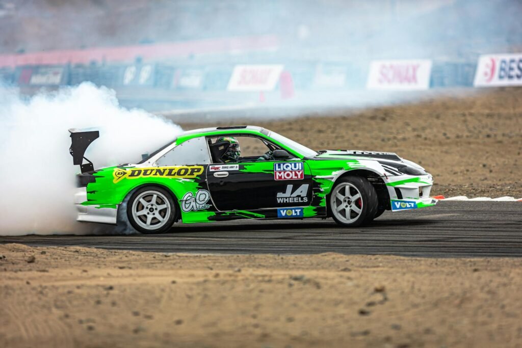 High-adrenaline shot of a green drift car speeding on a track, producing thick smoke.