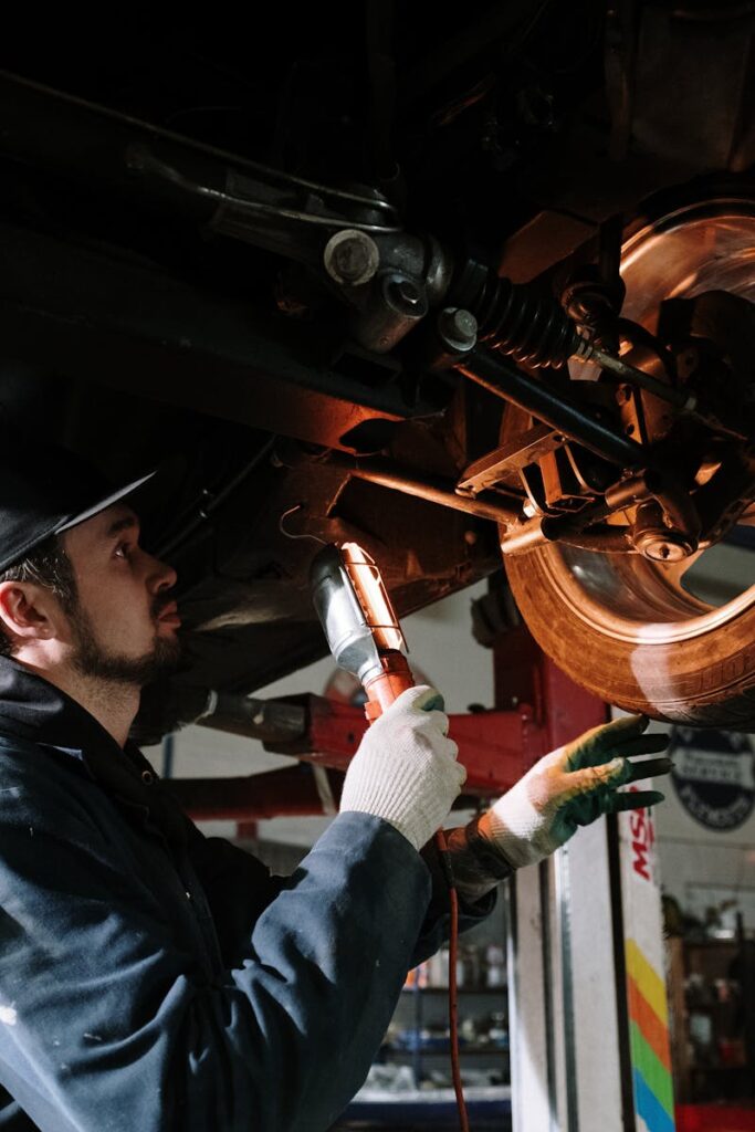 Mechanic uses a flashlight to inspect car's suspension in a garage setting.