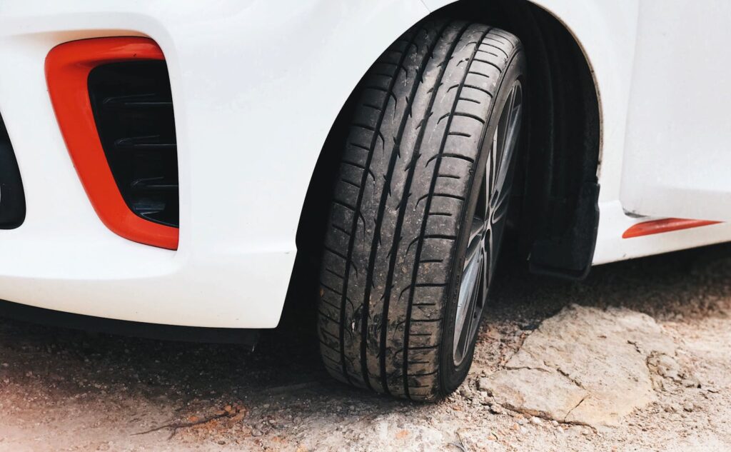 Detailed view of a white car's tire on a rocky surface, highlighting its tread and design.