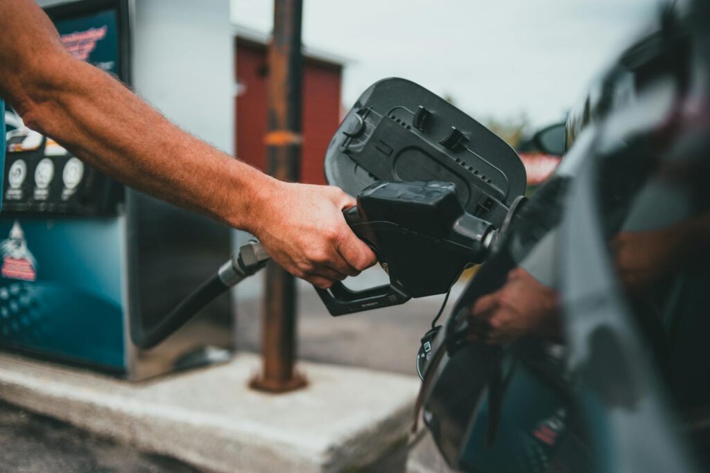 Close-up of a hand holding a nozzle while refueling a car at a gas station.