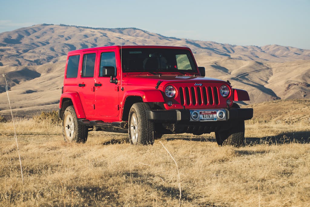 A striking red Jeep Wrangler parked in a vast, desert-like landscape under a clear sky.