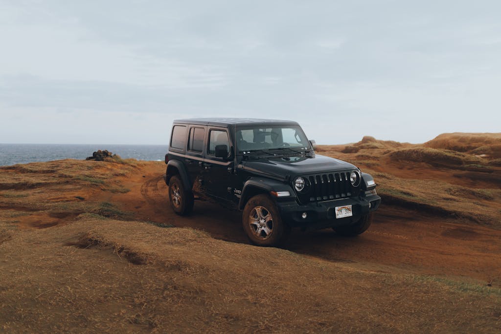 Jeep Wrangler off-roading on rugged terrain by the ocean, showcasing adventure and freedom.