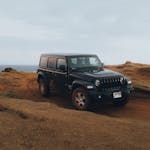 Jeep Wrangler off-roading on rugged terrain by the ocean, showcasing adventure and freedom.